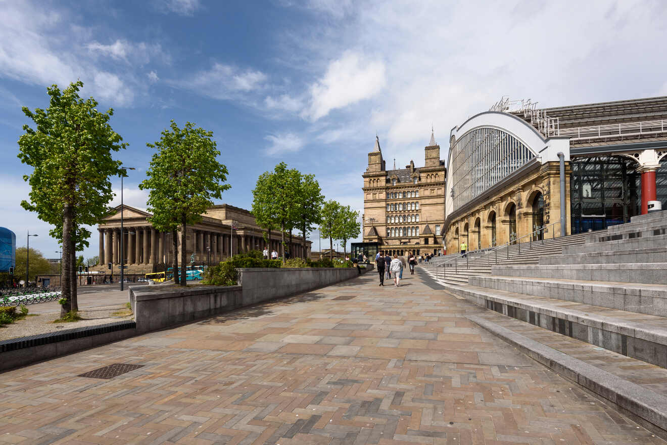 A view of Liverpool's Lime Street, featuring the neoclassical St George's Hall, with people walking along the wide pedestrian area under a partly cloudy sky